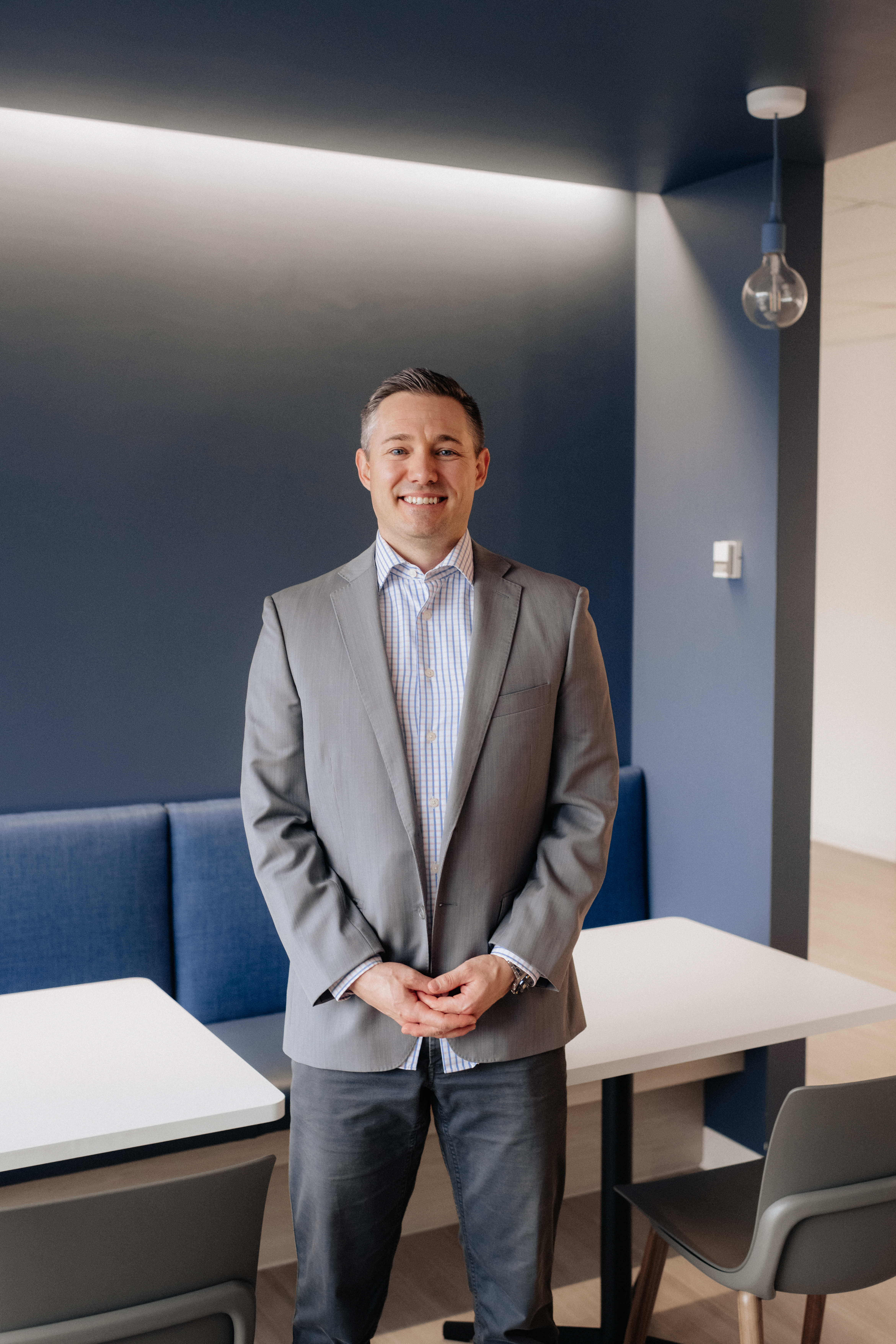 Ryan van der Hoorn smiling in a grey blazer against a navy office wall